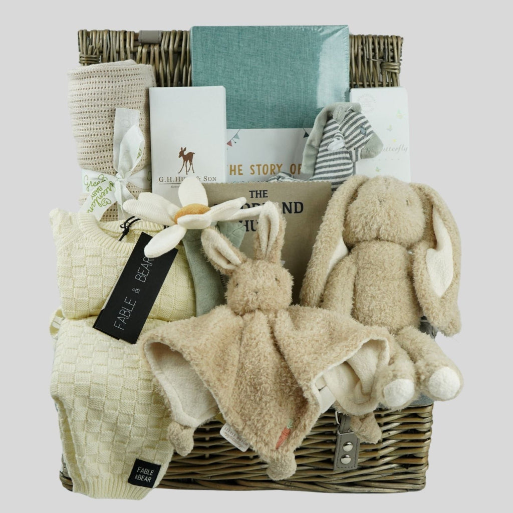 neutral baby hamper basket with caramel coloured organic cellular blanket, fabe and bear cream basket weave pattern baby 2 piece cream clothing set, bunny soft toy and matching baby comforter, luxury baby hairbrush, zebra stiped rattle, vavy diary, woodland rag book, organic baby bubble bath