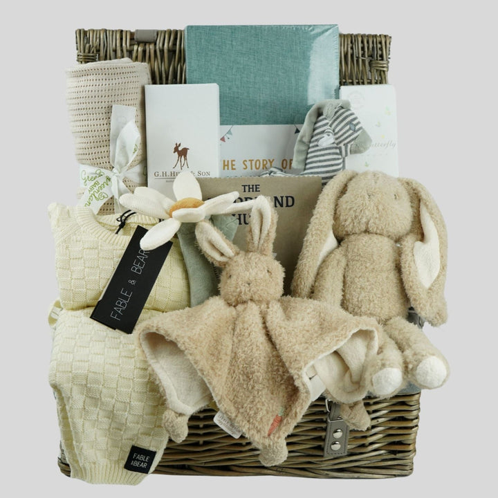 neutral baby hamper basket with caramel coloured organic cellular blanket, fabe and bear cream basket weave pattern baby 2 piece cream clothing set, bunny soft toy and matching baby comforter, luxury baby hairbrush, zebra stiped rattle, vavy diary, woodland rag book, organic baby bubble bath