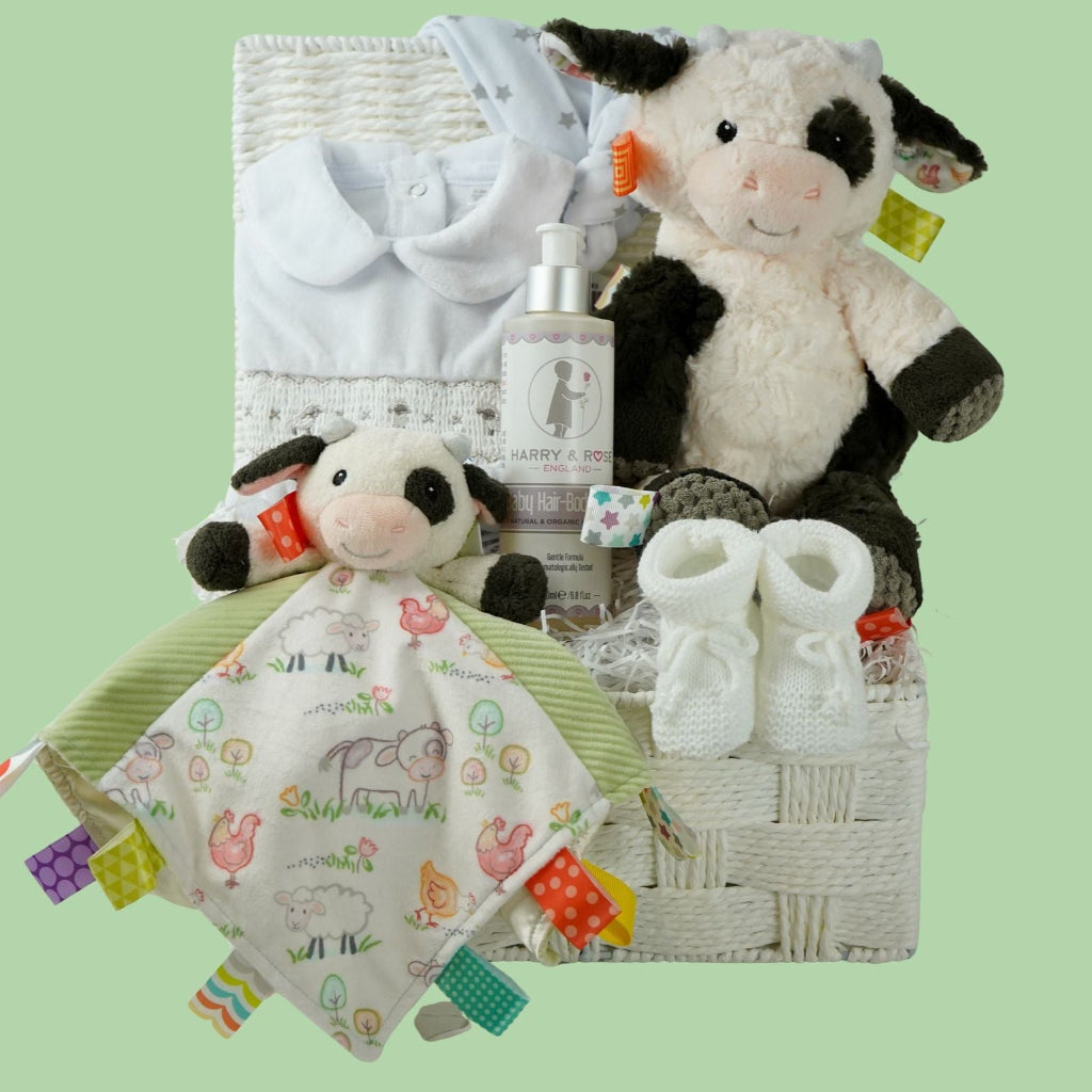 baby gift basket with a cow comforter and soft cow taggies toy, white baby sleepsuit with silver smocked sheep on bodice, organic toiletries, white knit booties and white with silver stars knot hat