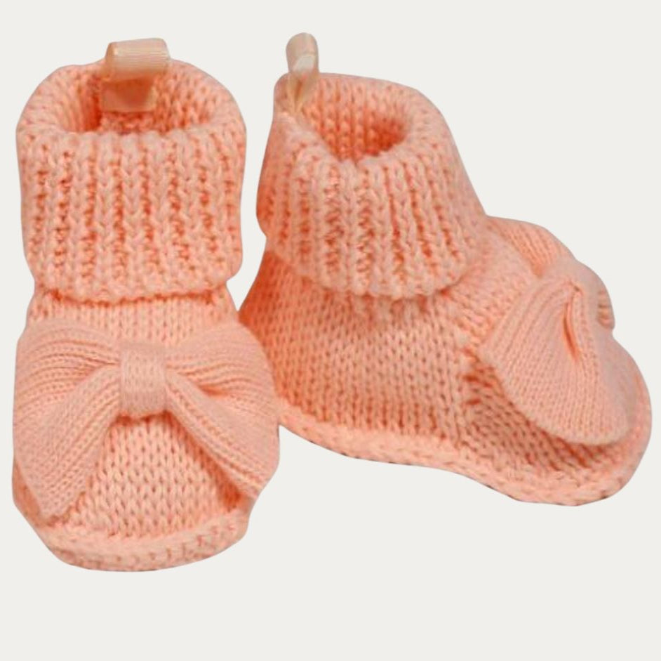 Pair of pink knitted baby booties with a bow on a light gray background