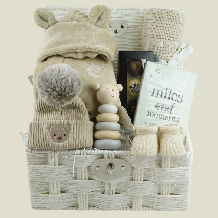 neutral baby gift with beige baby dressing gown, bamboo baby cellular blanket in beige, beige baby hat with teddy face, milestone baby cards, beige baby booties, wooden stacking toy,  chocolate