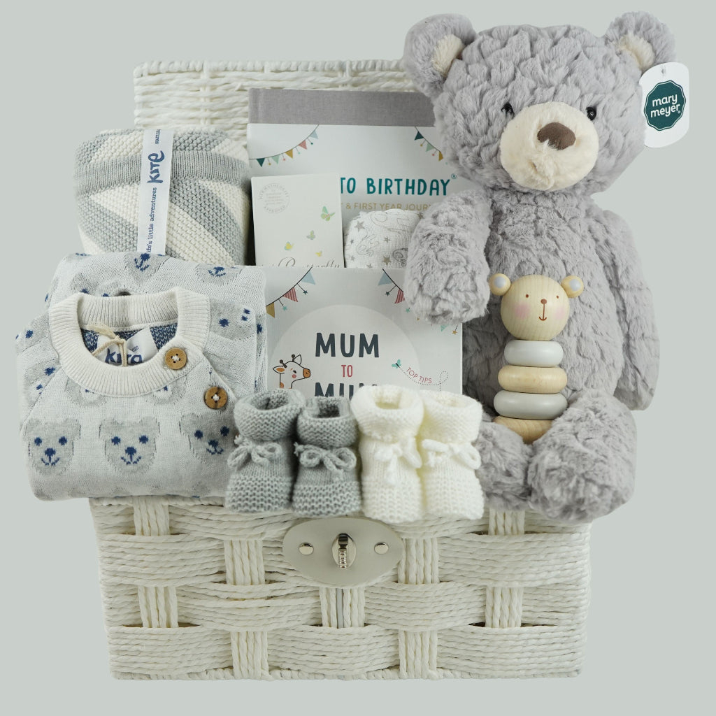 luxury baby gifts in white basket baby journal, organic baby blanket, organic snow bear baby romper, 2 pairs of baby booties, muslin, wooden staging toy and grey soft baby bear