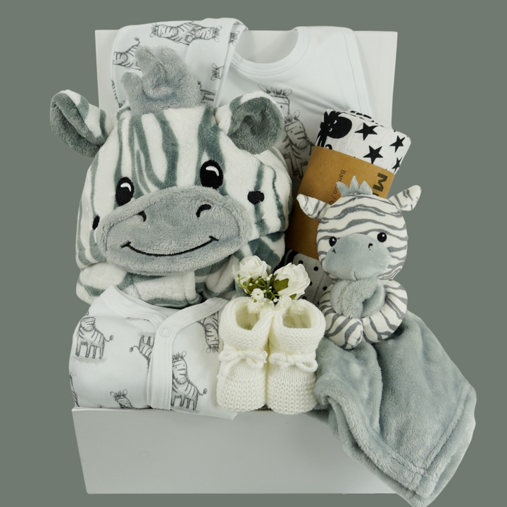 white hamper box with baby dressing gown with zebra faced hood, white baby sleepsuit with zebras, white baby hat with zebras, grey and white baby comforter with a zabra head, white knit baby booties, black and white sensory muslin swaddle  and