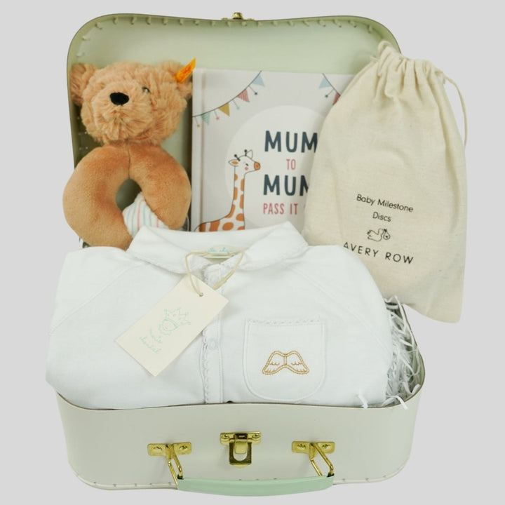 Luxury baby hamper in a Marie Chantal pale green suitcase,  white prima cotton baby sleepsuit with gold angel wings embroidered on the pocket, pregnancy milestone discs in a drawstring bag, mum to mum book, steiff teddy rattle
