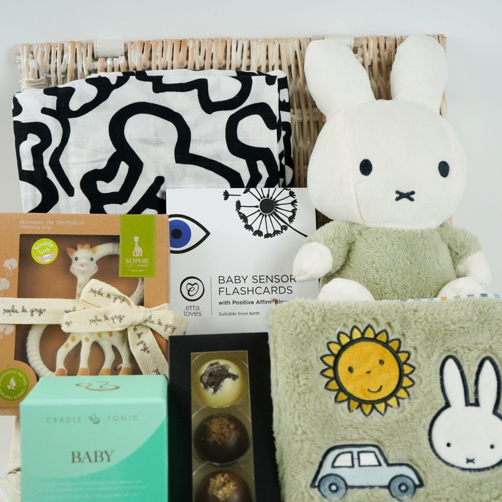White hamper basket with baby sensory muslin, baby sensory flash cards, Sophie la Giraffe teether, Miffy soft toy, Miffy soft activity book in Green, Aromatherapy candle, chocolates
