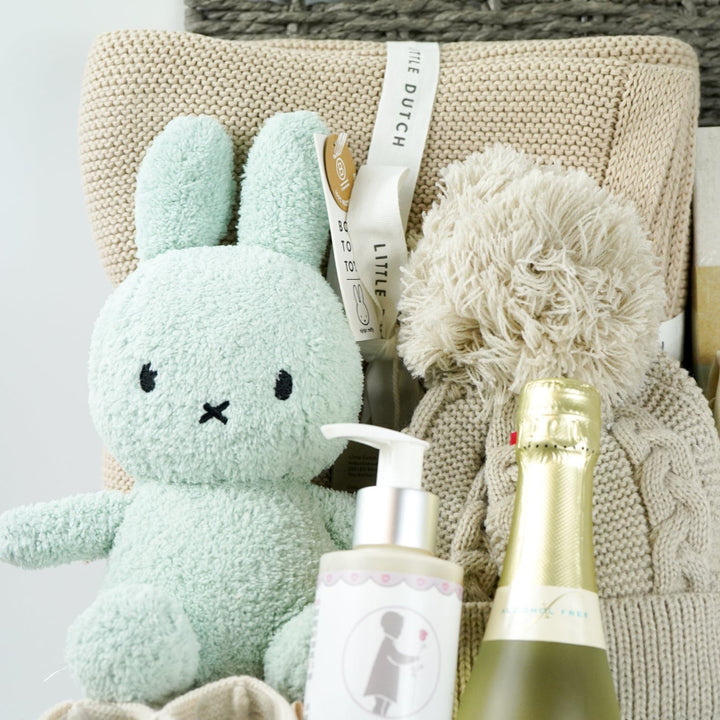 grey hamper baby basket with light green miffy, organic beige blanket, organic baby pompom hat, Little Dutch baby milestone cards, biscuit coloured nit booties, organic baby wash, mify organic clothing set includes a long sleeved tshirt, knit leggings with miffy on the bum, miffy socks , non alcoholic prosecco