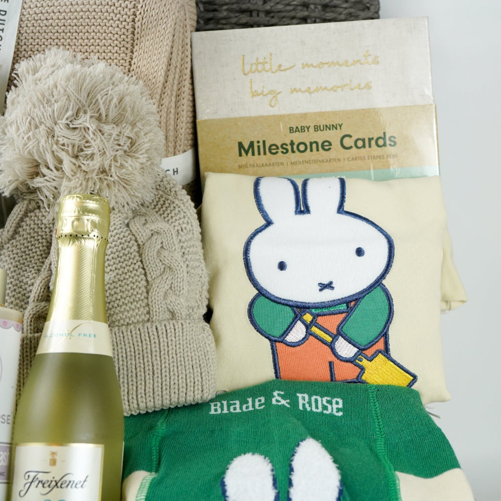 grey hamper baby basket with light green miffy, organic beige blanket, organic baby pompom hat, Little Dutch baby milestone cards, biscuit coloured nit booties, organic baby wash, mify organic clothing set includes a long sleeved tshirt, knit leggings with miffy on the bum, miffy socks , non alcoholic prosecco