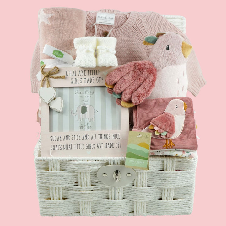 luxury baby girl hamper in mainly pink and white includes soft stroller book with a pink bird, butterflies and caterpillar theme, pink bird soft toy, white knit baby booties, dusky pink reversible baby blanket and pink baby girl picture frame and a pink baby girl cardigan in a white paper rope hamper basket