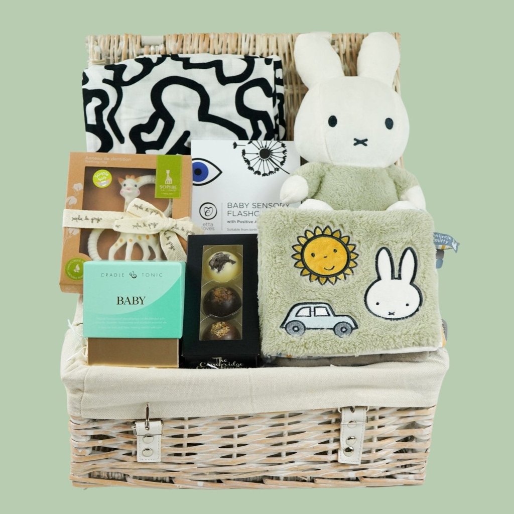 White hamper basket with baby sensory muslin, baby sensory flash cards, Sophie la Giraffe teether, Miffy soft toy, Miffy soft activity book in Green, Aromatherapy candle, chocolates