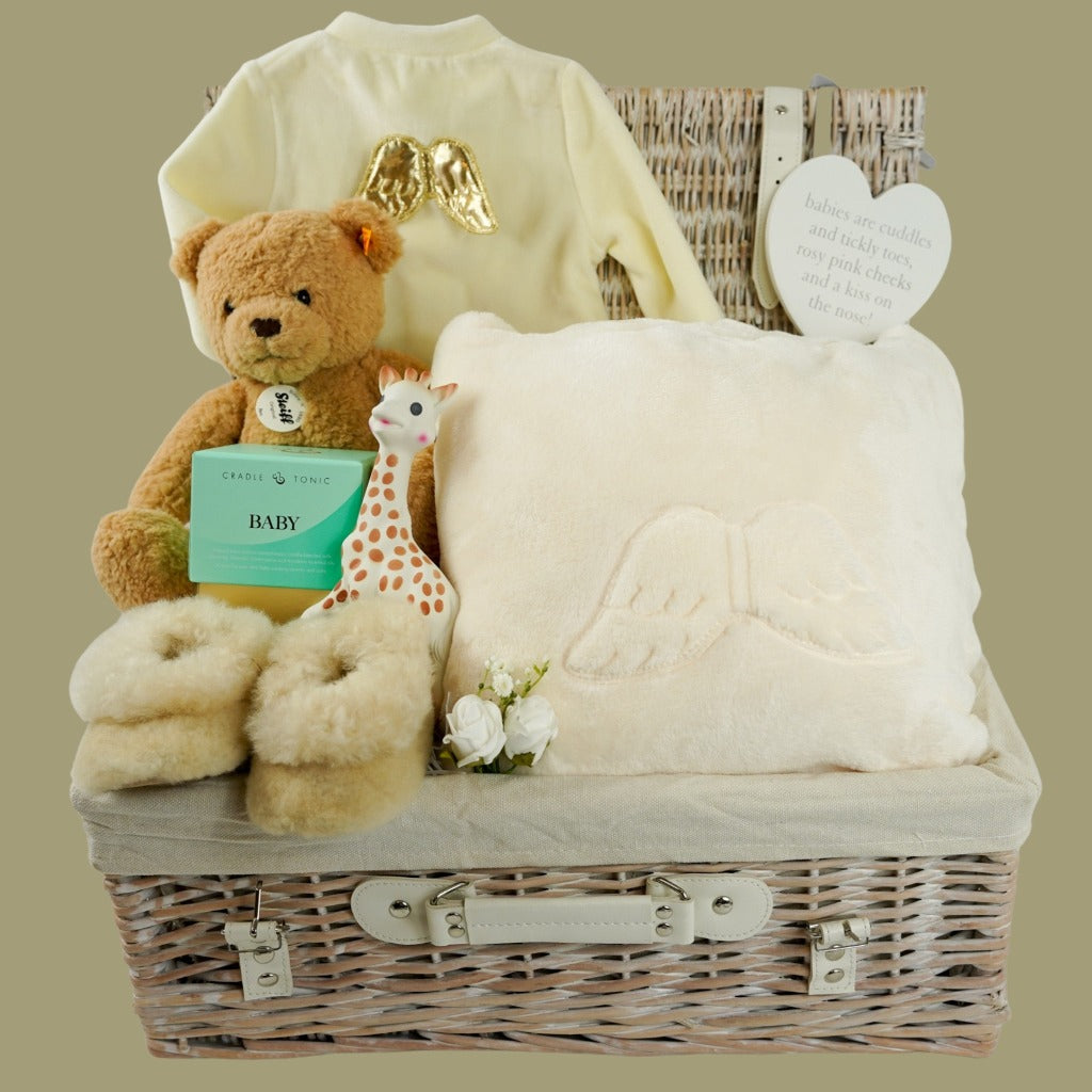 Luxury wicker baby and new mum hamper, cream velour baby sleepsuit with gold angel wings on the back, luxury ladies cream dressing gown with angel wings on the back, sophie la girafe teething toy, luxury alpaca baby slippers, luxury mother and baby candle, Steiff honey coloured teddy ben