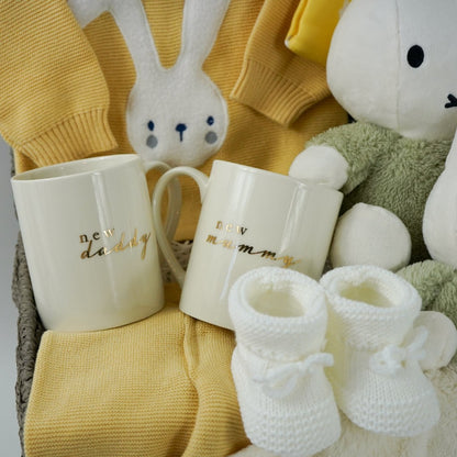 baby hamper in yellow organic knit with a white bunny face, White Miffy soft toy with green fluffy outfit and matching Miffy comforter , Cream bone china new mummy and new daddy mugs, yellow hat with cute ears and bunny , white booties