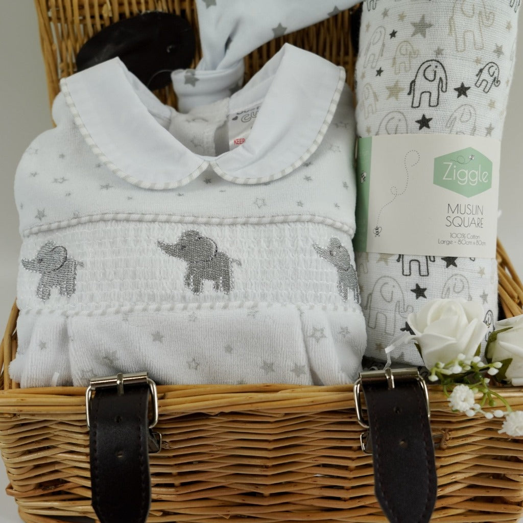 Small wicker basket, white velour baby sleepsuit with stars and grey elephants with a smocked front, white muslin with grey elephants, white cotton baby knot hat with silver stars