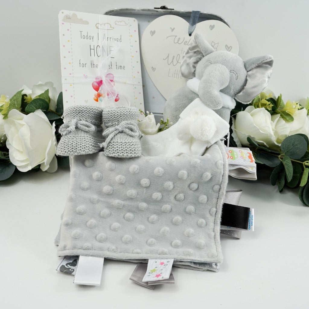grey and white baby case wioth memorable moments cards, grey taggie comfort blanket, grey knitted booties, white baby socks with pom poms, grey soft elephant rattle, white and sliver baby nursery plaque