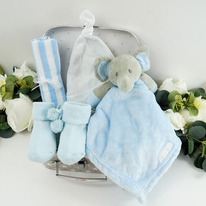 small baby hamper in a grey and white gift case, blue muslin, blue socks with pom poms and cute writing on the sole, baby knot hat in white , soft blue and grey baby elephant comforter