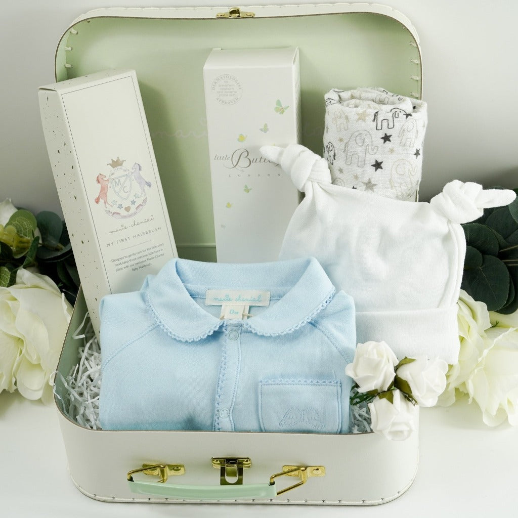 baby storage case with luxury designer baby sleepsuit in pale blue with a picot edge, baby double knot white cotton hat , ziggle muslin in white with grey and black elephants and stars, butterly London baby toiletries in a white box with butterfly design, Marie Chantal baby soft bristle hairbrush in keepsake box