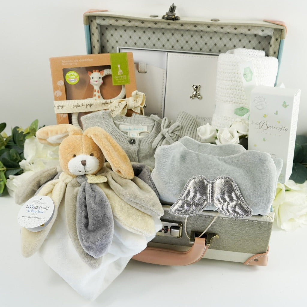 Blue, cream, grey stripe childs keepsake suitcae with luxury baby items including a rabbit comforter in grey, cream and white, sophie la giraffe teether, Luxury grey cashmere mix baby cardigan, baby passport holder and luggae tag in white with a silver plated teddy, velour baby sleepsuit  with angel wings in silver, organic baby toiletries