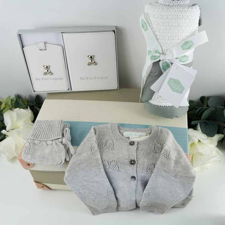 Blue, cream, grey stripe childs keepsake suitcae with luxury baby items including a rabbit comforter in grey, cream and white, sophie la giraffe teether, Luxury grey cashmere mix baby cardigan, baby passport holder and luggae tag in white with a silver plated teddy, velour baby sleepsuit with angel wings in silver, organic baby toiletries