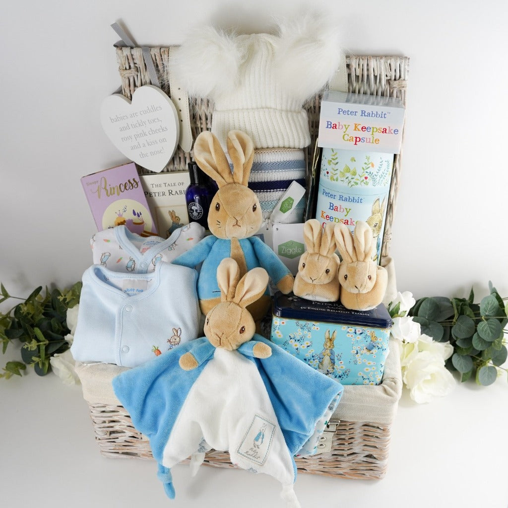 Luxury baby hamper with Peter rabbit itmes including Peter Rabbit soft toy, Peter rabbit baby comforter in blue and white, Soft brown Peter Rabbit baby slippers, Peter Rabbit Time Capsule, Peter Rabbit Book, Peter Rabbit baby clothing set including a pale blue jacket with Peter Rabbit embroidered, Luxury chocolate bar, collectors Peter Rabbit tin with breakfast tea, Soft blue and beige stripe heavy knit baby blanket, Neals yard baby toiletries