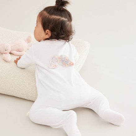 White velour baby sleepsuit with liberty print ruffle collar and libertiy print wings and trims around the cuffs, the sleepsuit is a soft velour