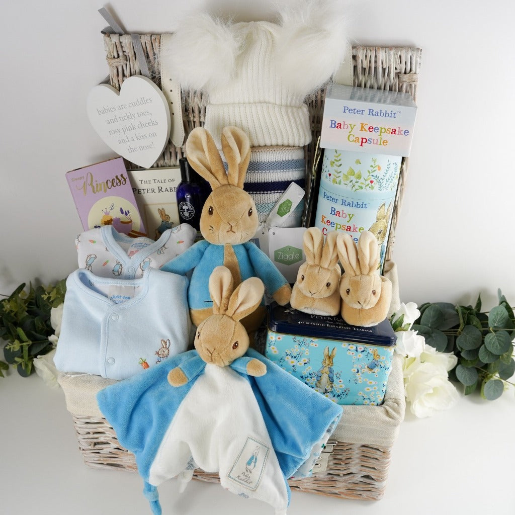 Luxury baby hamper with Peter rabbit itmes including Peter Rabbit soft toy, Peter rabbit baby comforter in blue and white, Soft brown Peter Rabbit baby slippers, Peter Rabbit Time Capsule, Peter Rabbit Book, Peter Rabbit baby clothing set including a pale blue jacket with Peter Rabbit embroidered, Luxury chocolate bar, collectors Peter Rabbit tin with breakfast tea, Soft blue and beige stripe heavy knit baby blanket, Neals yard baby toiletries