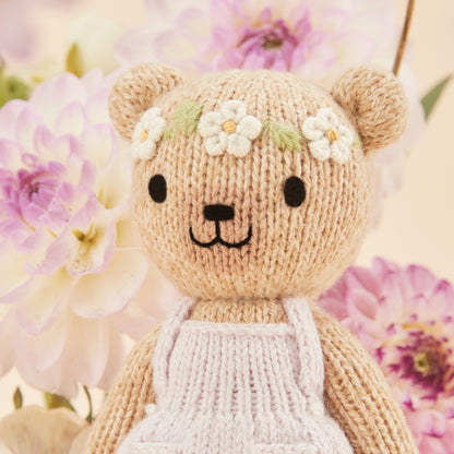 Knitted teddy bear with a floral headband next to a decorative box with floral patterns