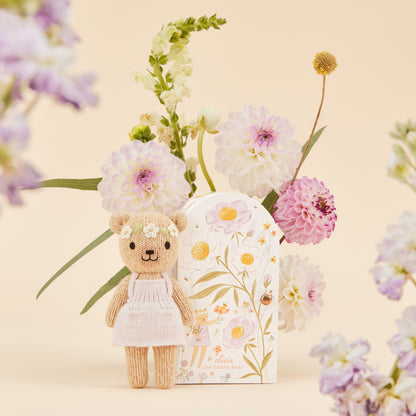 Knitted teddy bear with a floral headband next to a decorative box with floral patterns
