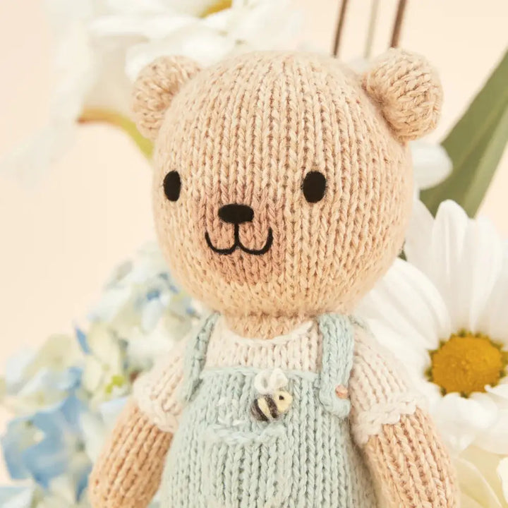 tiny charlie hand knitted bear in pale blue dungaree's with a honey bee