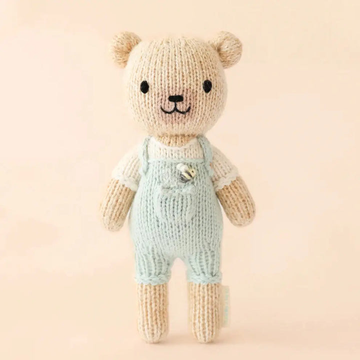 tiny charlie hand knitted bear in pale blue dungaree's with a honey bee
