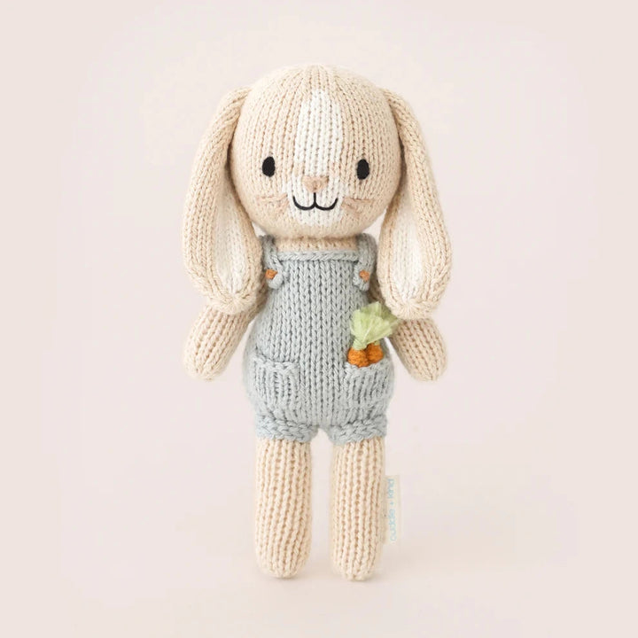 Knitted toy rabbit with a carrot in his pocket and light blue dungarees