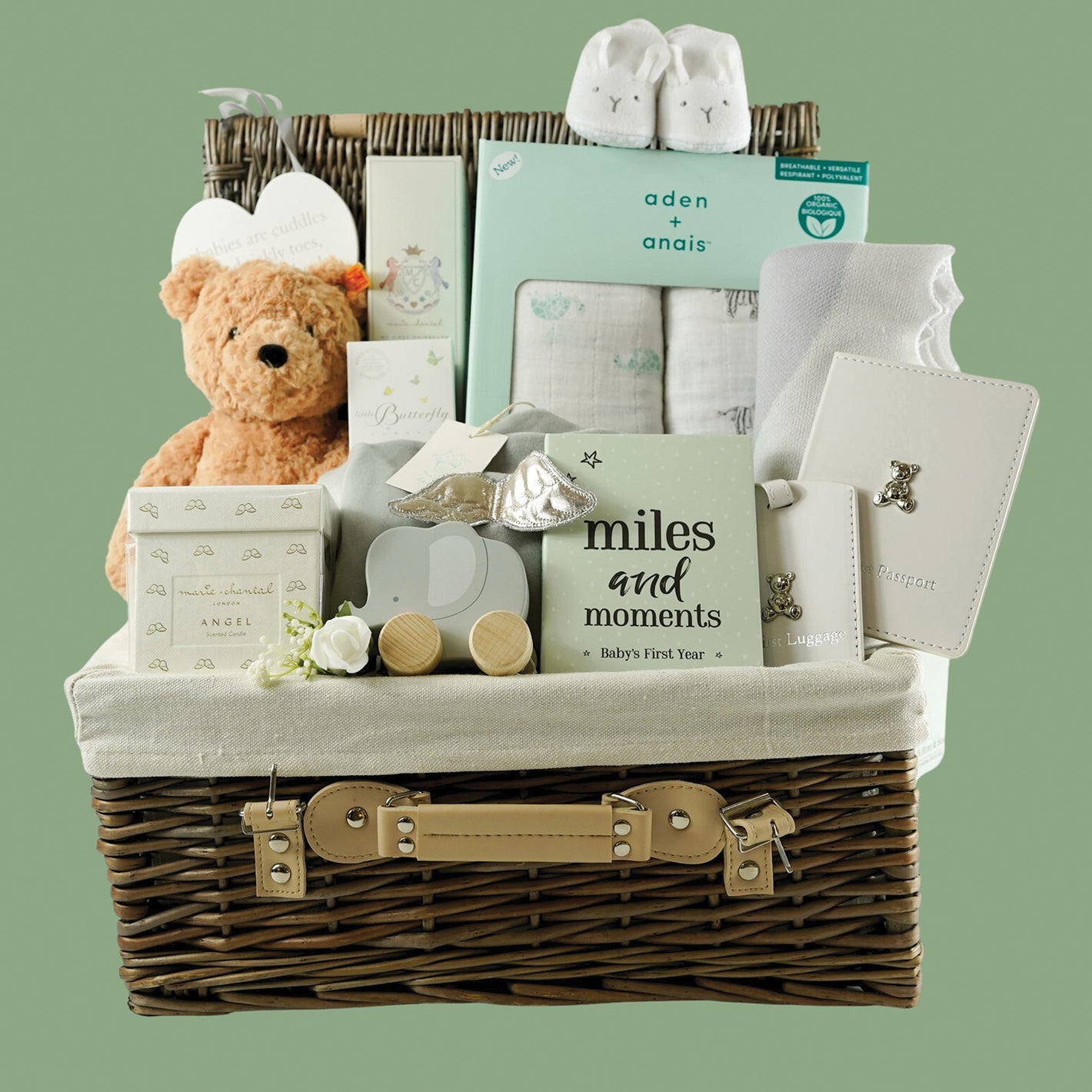 Hamper basket with luxury baby velour sleepsuit, luxury Marie Chantal candle, Baby muslin swaddles, baby luggage label and baby passport holder, Steiff teddy bear, soft natural baby hairbrush