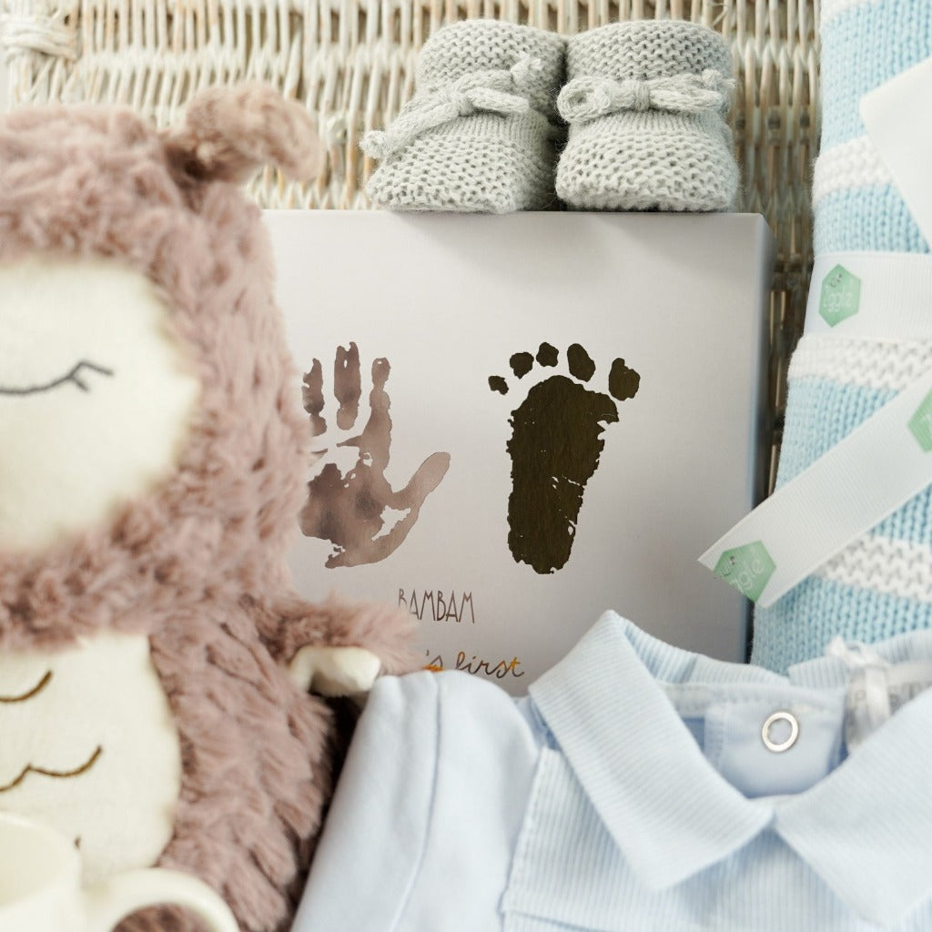 wicker basket, baby boy blue striped romper with a collar, Steiff owl soft toy, baby hand and footprint set, blue and white striped blanket, baby bootees, mummy mug
