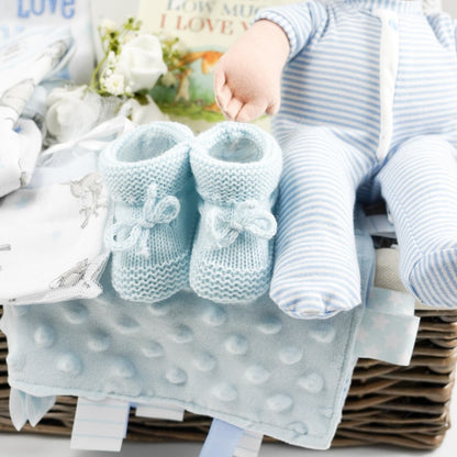 Wicker hamper with white baby set with Guess How Much I Love you Rabbit, baby rag doll in blue and white romper, grey cellular blanket, muslin , baby booties in pale blue with tie, organic baby toiletries