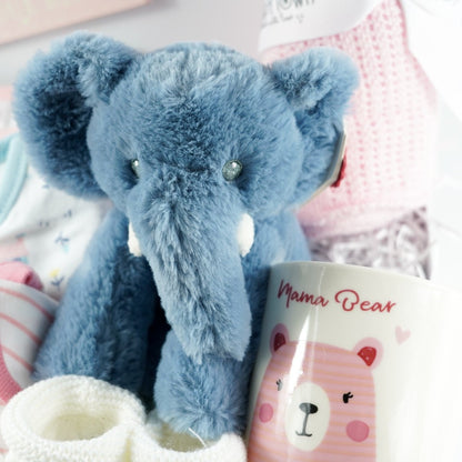 white magnetic hamper box with baby girl gifts , 3 bodysuits in oragnic cotton in pink, blue and white with little houses design, soft blue elephant plus and matching elephant comforter, white baby booties, pink baby cellular blanket, mama mug, baby pink nursery plaque