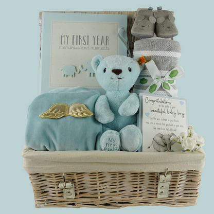 White wicker  basket, angel wings blue velour  sleepsuit,  blue Steiff my first teddy, grey and white ziggle blanket, My first year record book