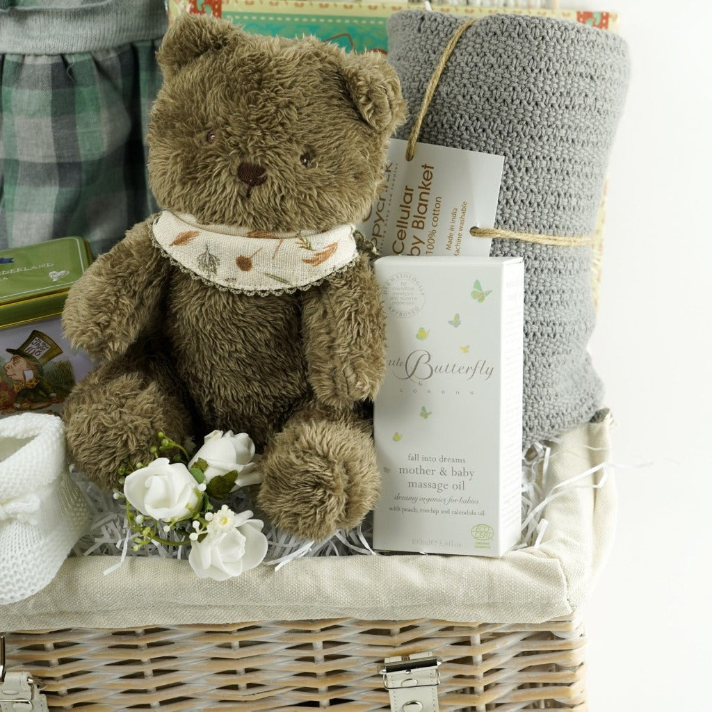 Wicker hamper basket with Calamaro grey and gren check baby romper, brown soft baby teddy bear, baby white booties, Alice in Wonderland tea caddy, grey cellular baby blanket, messages for you baby keepsake book, little butterfly London baby and mum toiletries