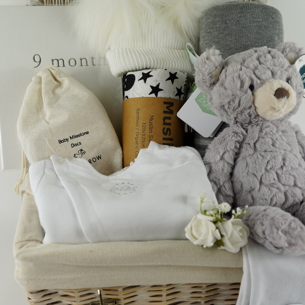 Pregnancy hamper basket with grey teddy, grey baby blanket with stars , black and white sensory baby swaddle, white baby hat with 2 Pom poms . White pregnancy journal. Pregnancy milestone discs, white baby clothing set includes jacket, bodysuit and leggings