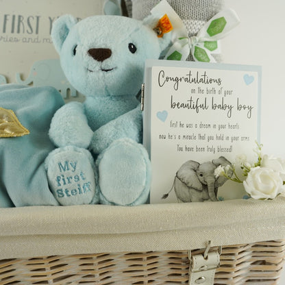White wicker basket, angel wings blue velour sleepsuit, blue Steiff my first teddy, grey and white ziggle blanket, My first year record book