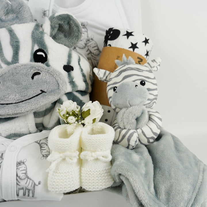 white hamper box with baby dressing gown with zebra faced hood, white baby sleepsuit with zebras, white baby hat with zebras, grey and white baby comforter with a zabra head, white knit baby booties, black and white sensory muslin swaddle and