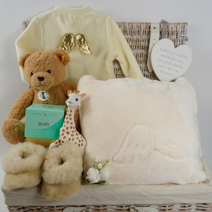 Luxury wicker baby and new mum hamper, cream velour baby sleepsuit with gold angel wings on the back, luxury ladies cream dressing gown with angel wings on the back, sophie la girafe teething toy, luxury alpaca baby slippers, luxury mother and baby candle, Steiff honey coloured teddy ben