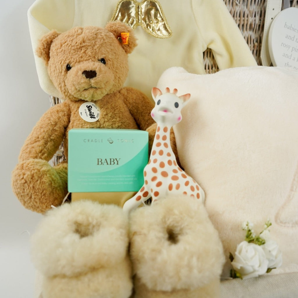 Luxury wicker baby and new mum hamper, cream velour baby sleepsuit with gold angel wings on the back, luxury ladies cream dressing gown with angel wings on the back, sophie la girafe teething toy, luxury alpaca baby slippers, luxury mother and baby candle, Steiff honey coloured teddy ben