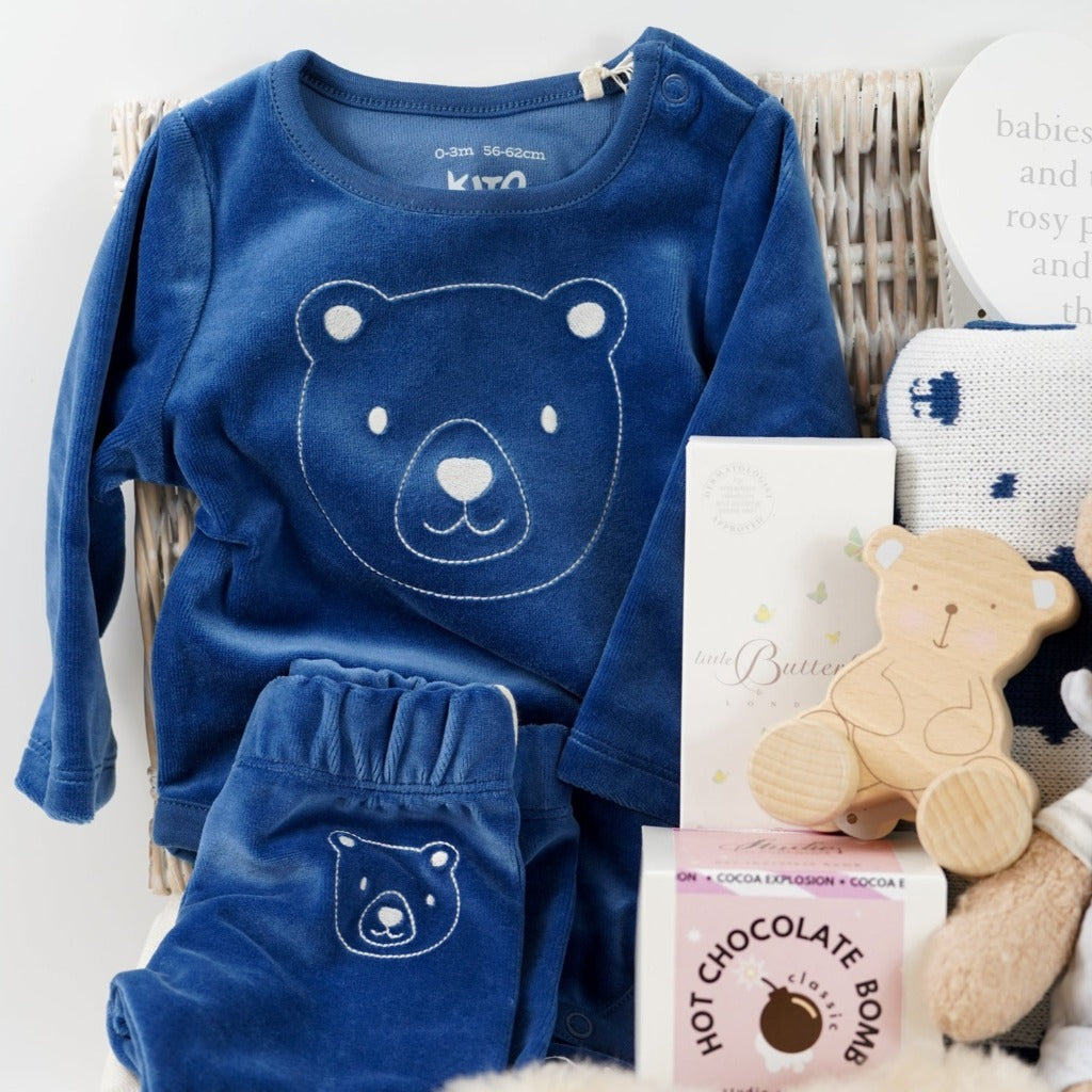 baby boy hamper with blue velour organic top and leggings, alpaca baby slippers, steiff organic bear, organic blue and white teddy bear blanket , wooden bear poush along toy , natural baby toiletries in a white wicker hamper basket