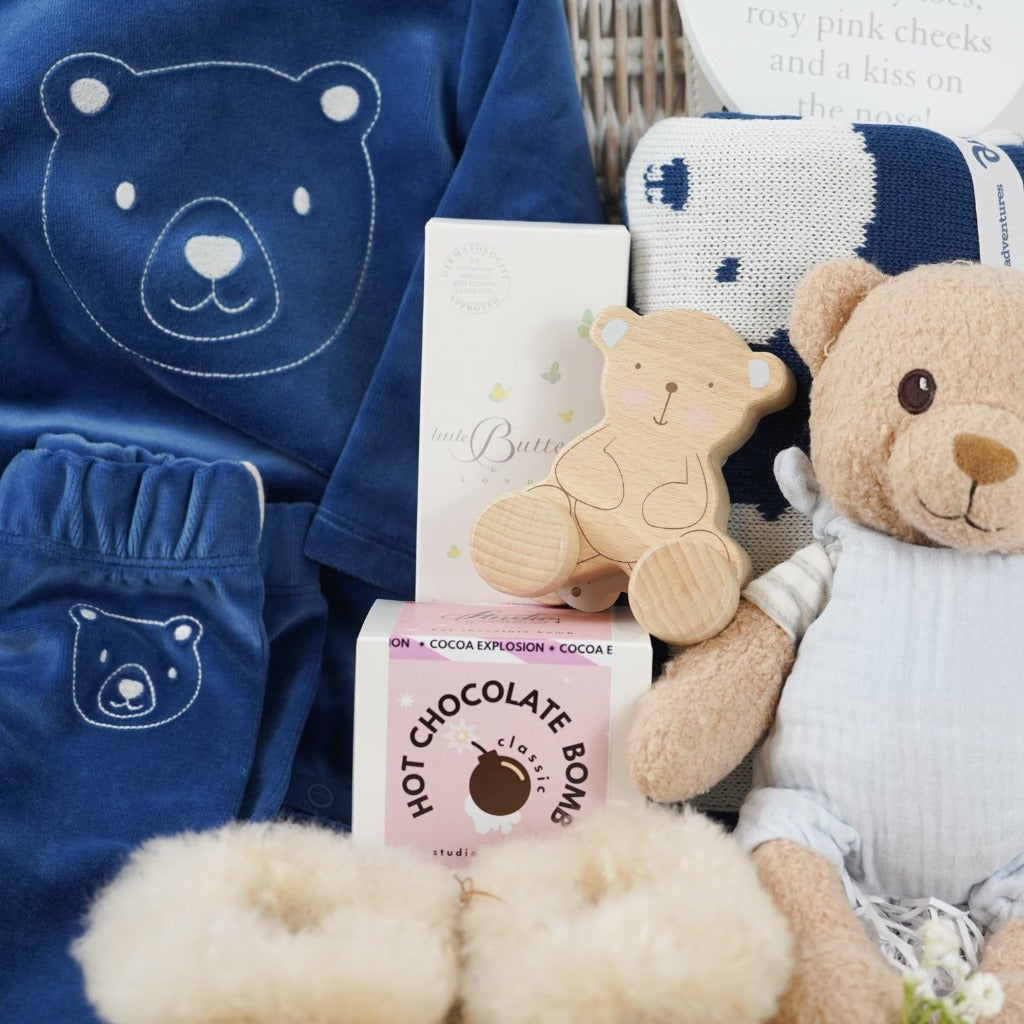 baby boy hamper with blue velour organic top and leggings, alpaca baby slippers, steiff organic bear, organic blue and white teddy bear blanket , wooden bear poush along toy , natural baby toiletries in a white wicker hamper basket