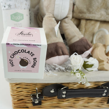 baby hamper in wicker basket with a fawn soft toy, white cotton cellular blanket, while soft large muslin with grey elephants and stars, soft fawn coloured dressing gown with cute teddy ears, white knit booties, set of wooden teething keys on a rope, hot chocolate bomb
