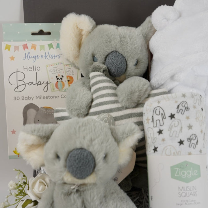 baby hamper box with white soft baby dressing gown in white with cute ears, Koala sofy comfort blanket in grey and white, baby milestone cards , muslin in white with grey elephants , white baby booties