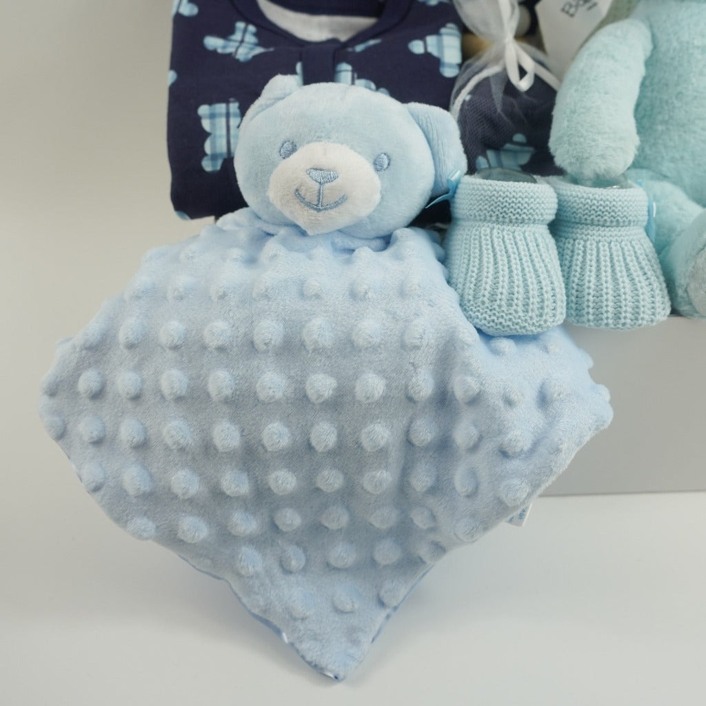 baby boy hamper includes blue layette baby clothing set in navy with tartan teddy pattern in lighter blue, blue knit booties, my first steiff teddy in blue with button in ear, wooden stacking toy, teddy dimple fleece baby comforter, white cellular blanket