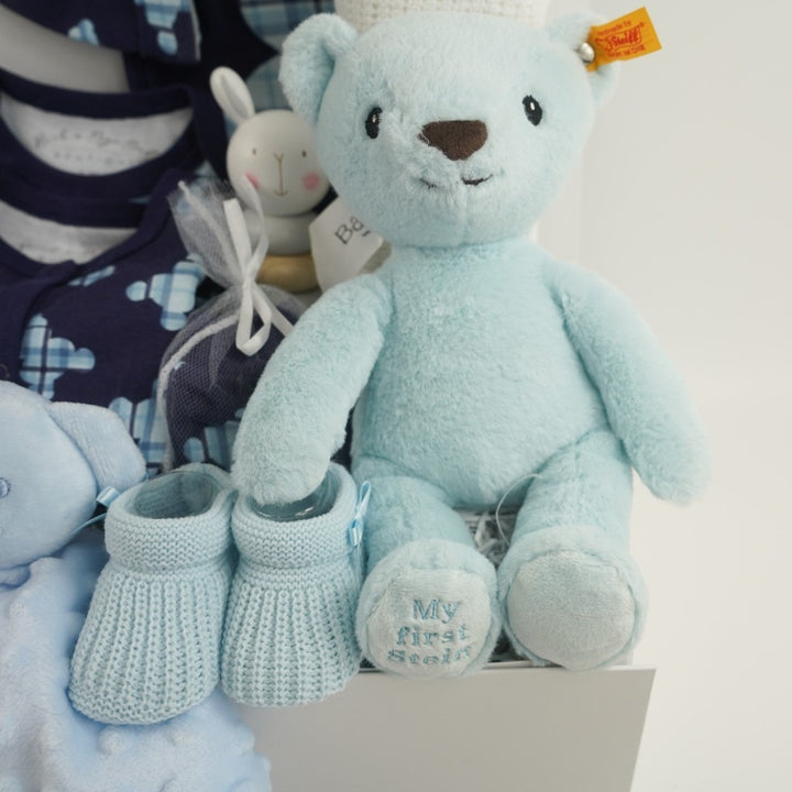 baby boy hamper includes blue layette baby clothing set in navy with tartan teddy pattern in lighter blue, blue knit booties, my first steiff teddy in blue with button in ear, wooden stacking toy, teddy dimple fleece baby comforter, white cellular blanke