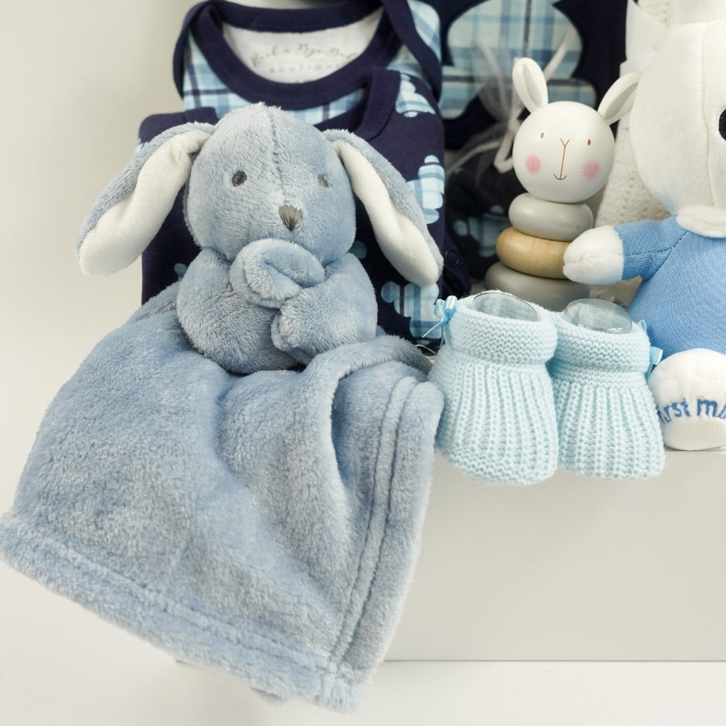 baby boy hamper includes navy baby layette with pale blue tartan teddy design includes a sleepsuit, bodysuit, hat, mittens and bib, white cotton cellular blanket, wooden rabbit stacking toy, dusky blue rabbit comforter, blue knit booties, My First Miffy white toy with a blue outfit