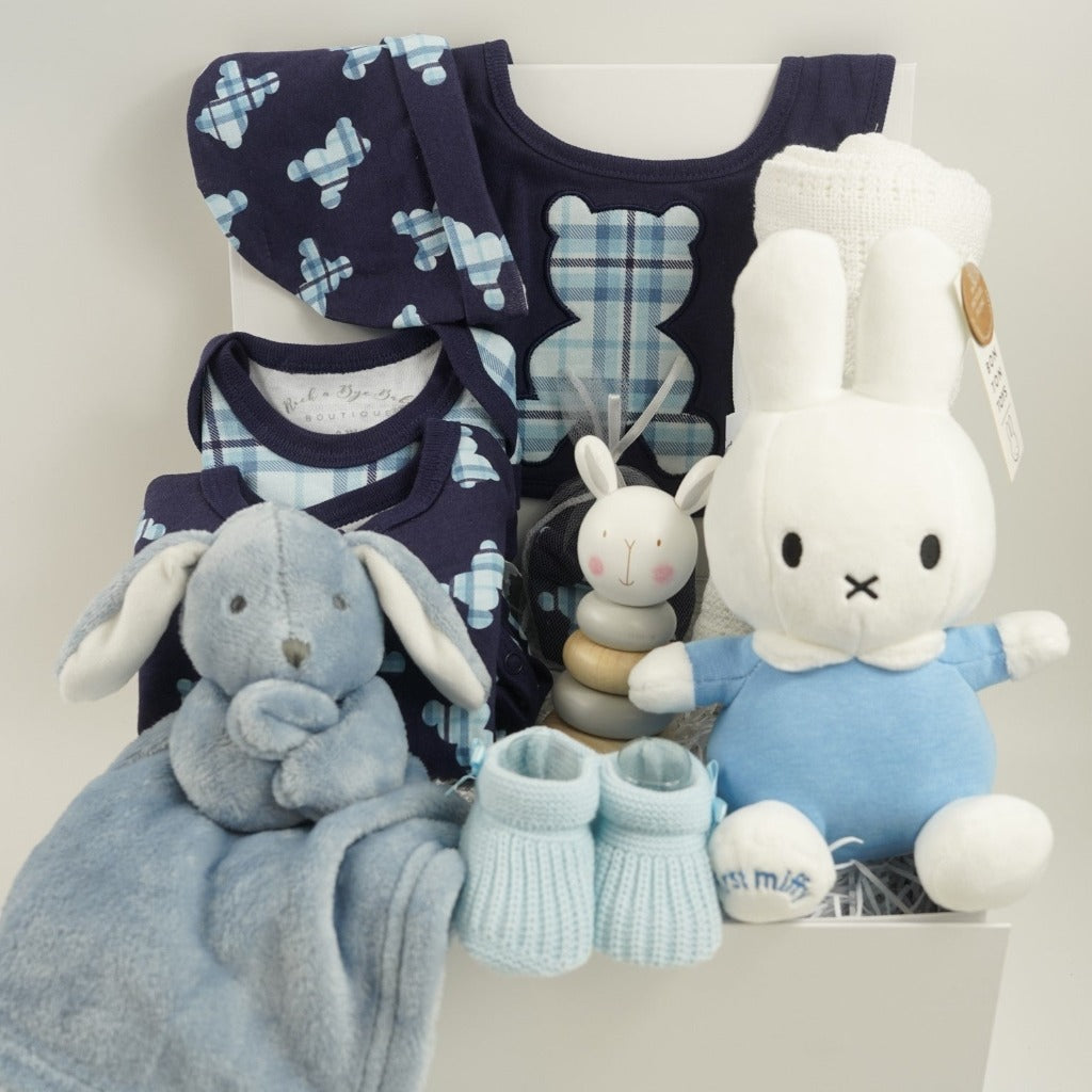 baby boy hamper includes navy baby layette with pale blue tartan teddy design includes a sleepsuit, bodysuit, hat, mittens and bib, white cotton cellular blanket, wooden rabbit stacking toy, dusky blue rabbit comforter, blue knit booties, My First Miffy white toy with a blue outfit