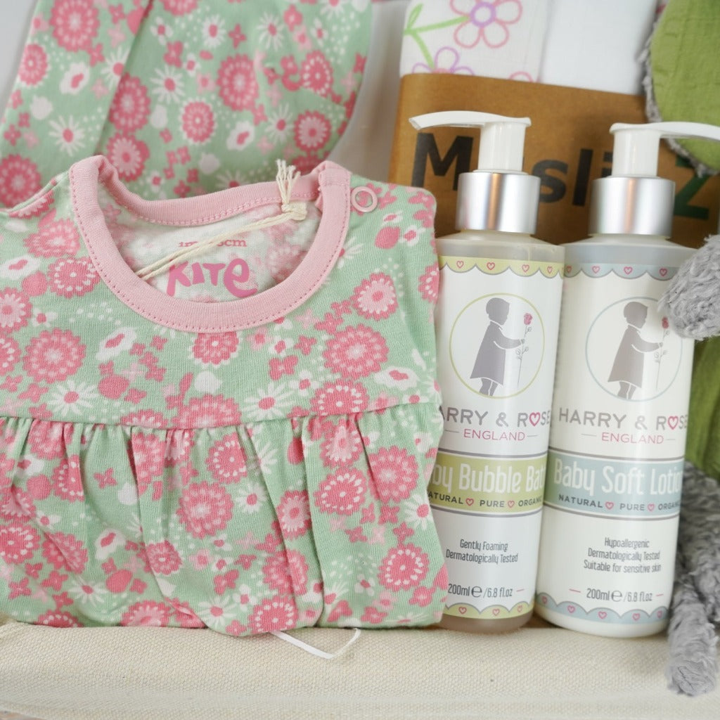 White hamper basket with baby girl organic gifts, pale green with pink flowers baby organic sleepsuit , matching organic hat, organic baby wash and body lotion, organic muslins in white with pink flowers, organic mouse soft toy, The story of us baby journal, motherhood 3 mini candles