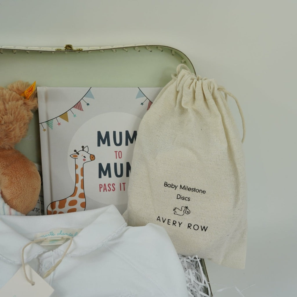 Luxury baby hamper in a Marie Chantal pale green suitcase, white prima cotton baby sleepsuit with gold angel wings embroidered on the pocket, pregnancy milestone discs in a drawstring bag, mum to mum book, steiff teddy rattle